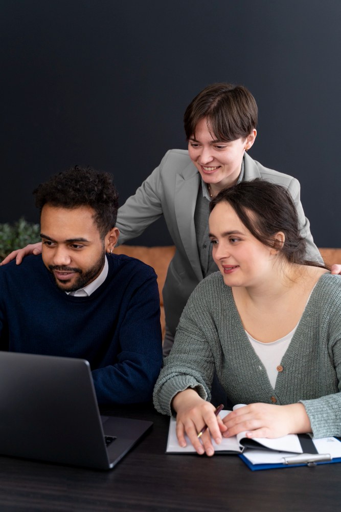 Three colleagues smiling at a laptop, one leaning in from behind